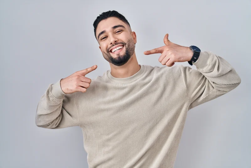A smiling man pointing toward his smile