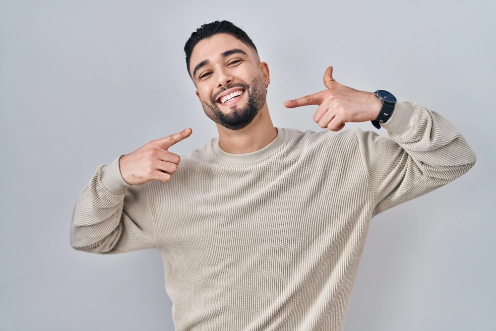 A smiling man pointing toward his smile